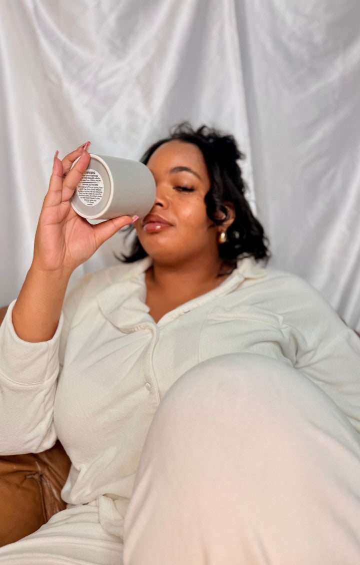 Asher-Leigh holding an Alluminate Aesthetics candle to her face, eyes closed, wrapped in cream loungewear